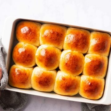 female hands holding a white pan filled with dinner rolls