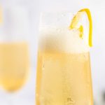 two champagne flutes with elderflower cocktail and lemon peel garnish