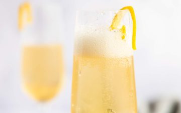 two champagne flutes with elderflower cocktail and lemon peel garnish