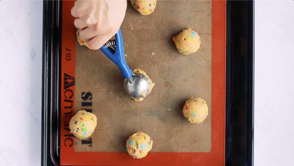 placing a cookie dough ball on a lined baking sheet