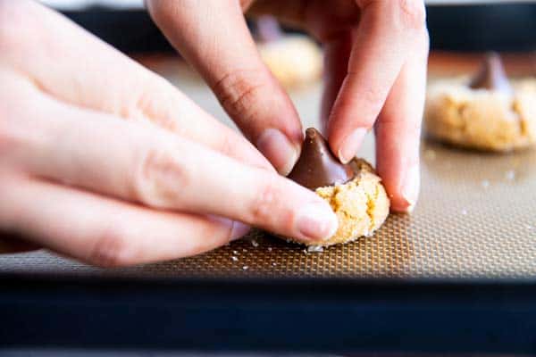 female hands pushing a chocolate kiss into a baked peanut butter cookie