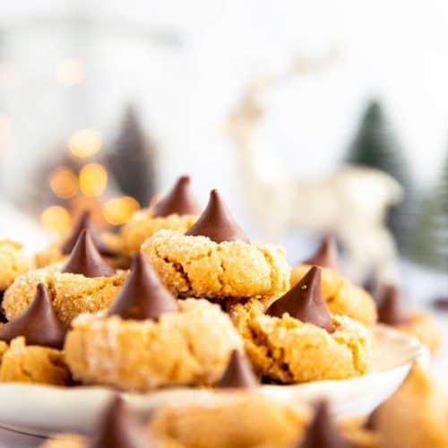 piles of peanut butter blossom cookies on a plate in front of festive decor