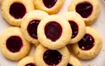 pile of shortbread thumbprint cookies on a cream colored plate