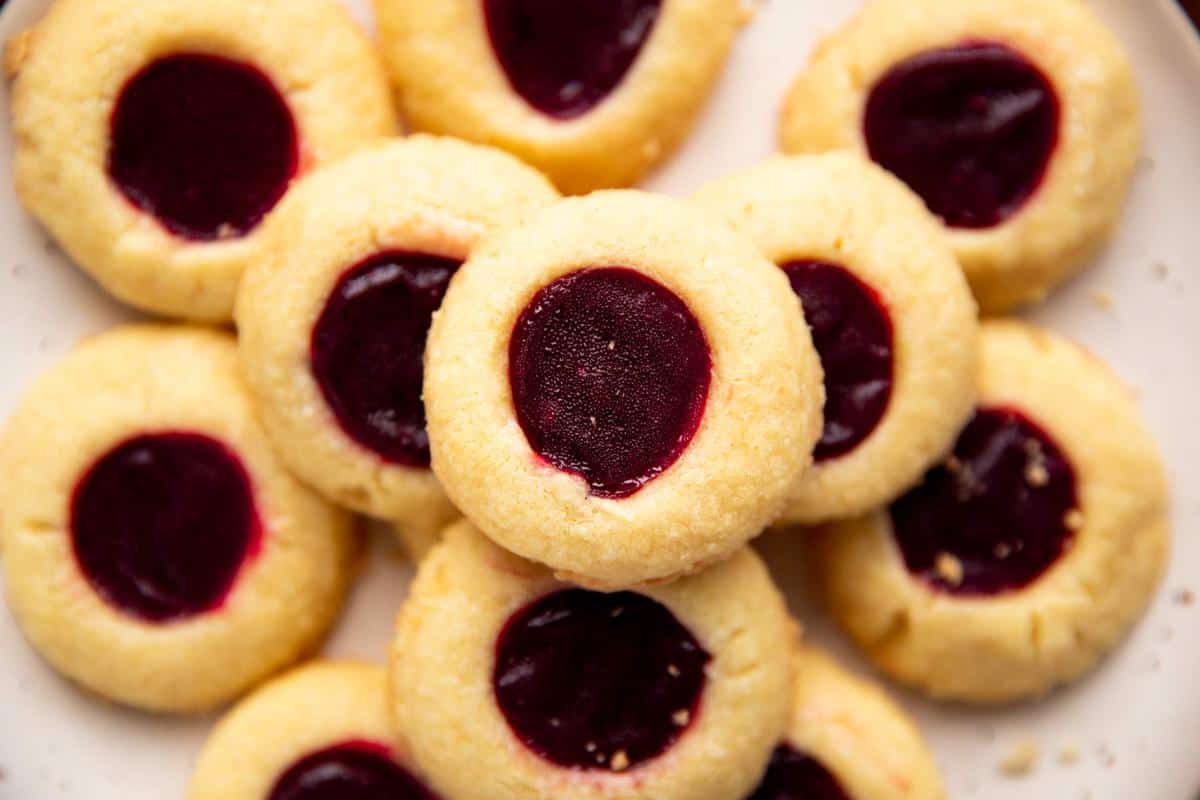 pile of shortbread thumbprint cookies on a cream colored plate