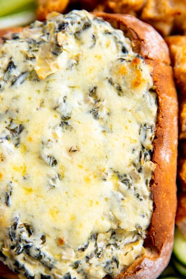 close up photo of a bread bowl filled with spinach artichoke dip