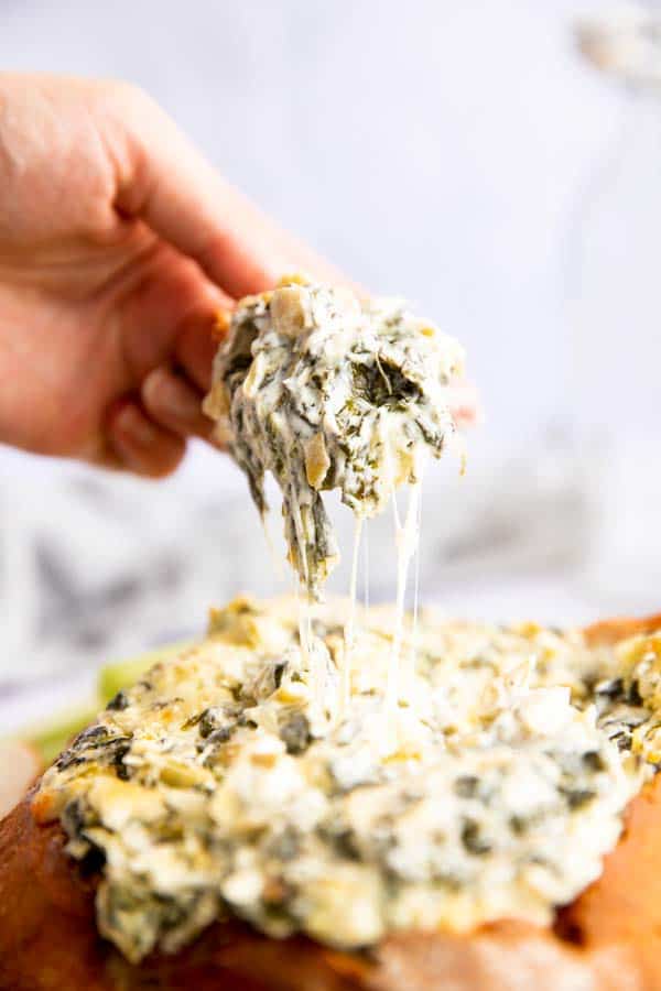 female hand dipping bread in spinach artichoke dip