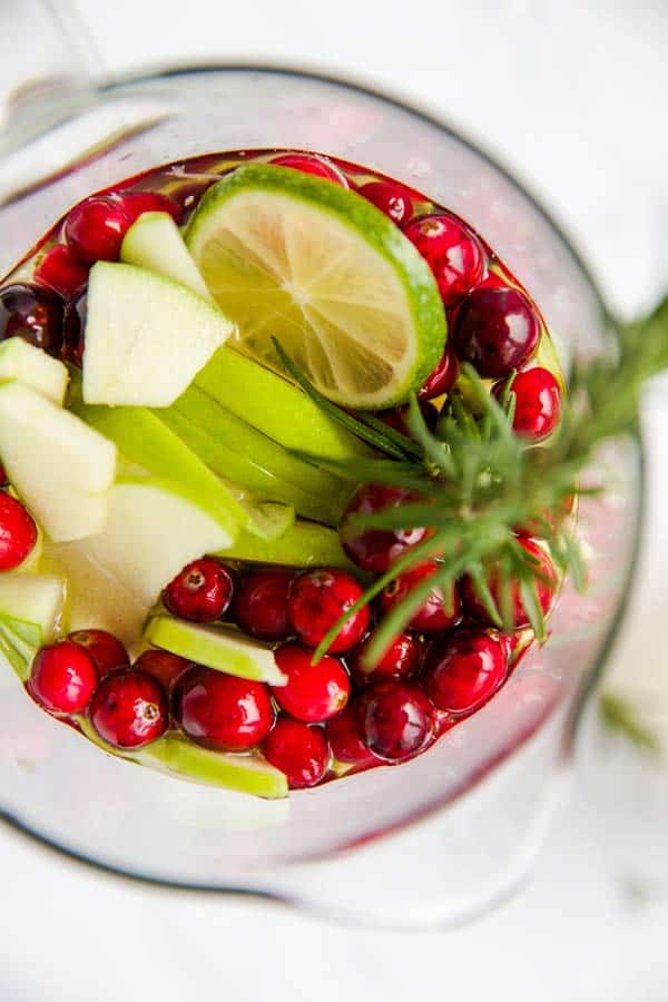 top down view on a pitcher with lime, apple, cranberries and rosemary