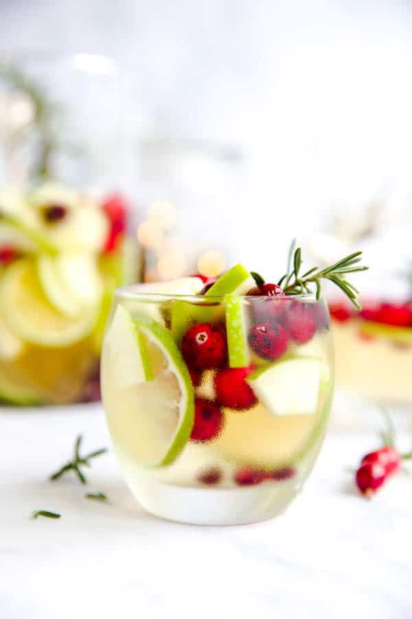 Tumblr with white sangria filled with apple, lime, pomegranate and cranberries