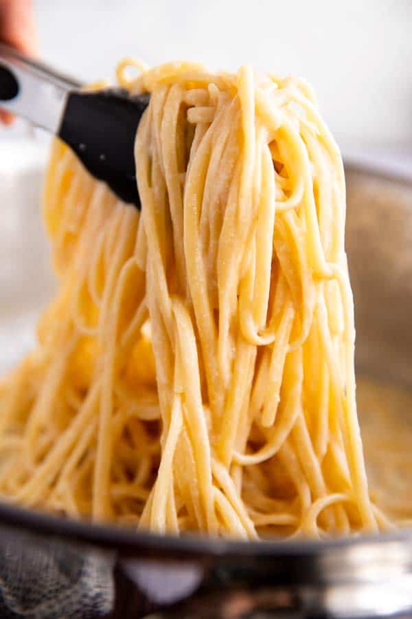 pulling up fettuccine Alfredo with kitchen tongs