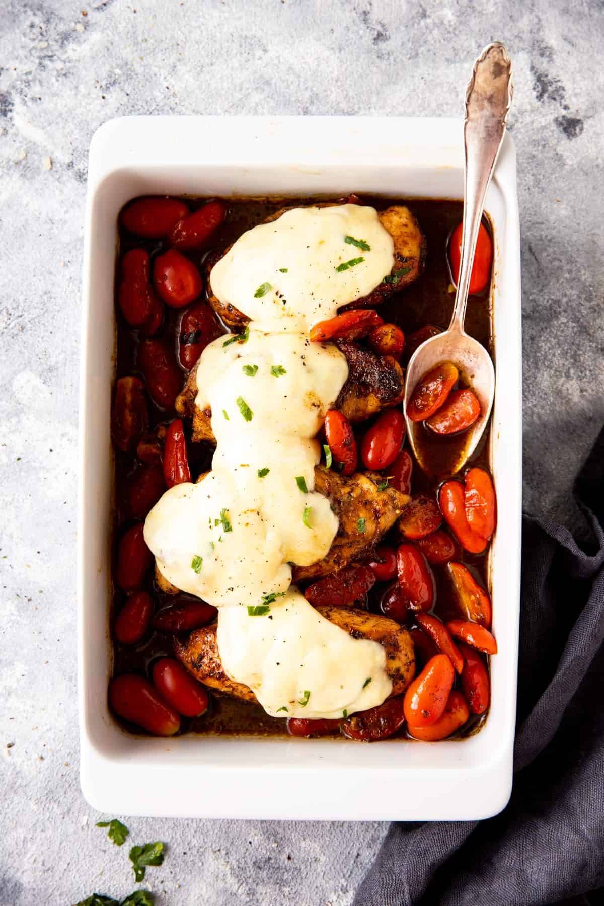 white casserole dish with chicken and tomatoes covered in mozzarella cheese