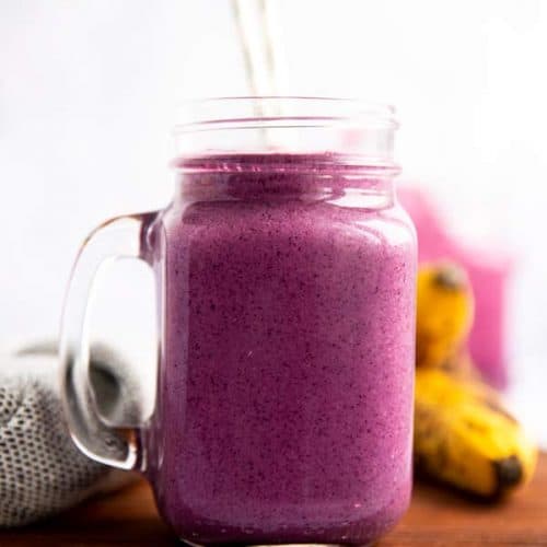 glass with purple blueberry banana smoothie on a wooden board
