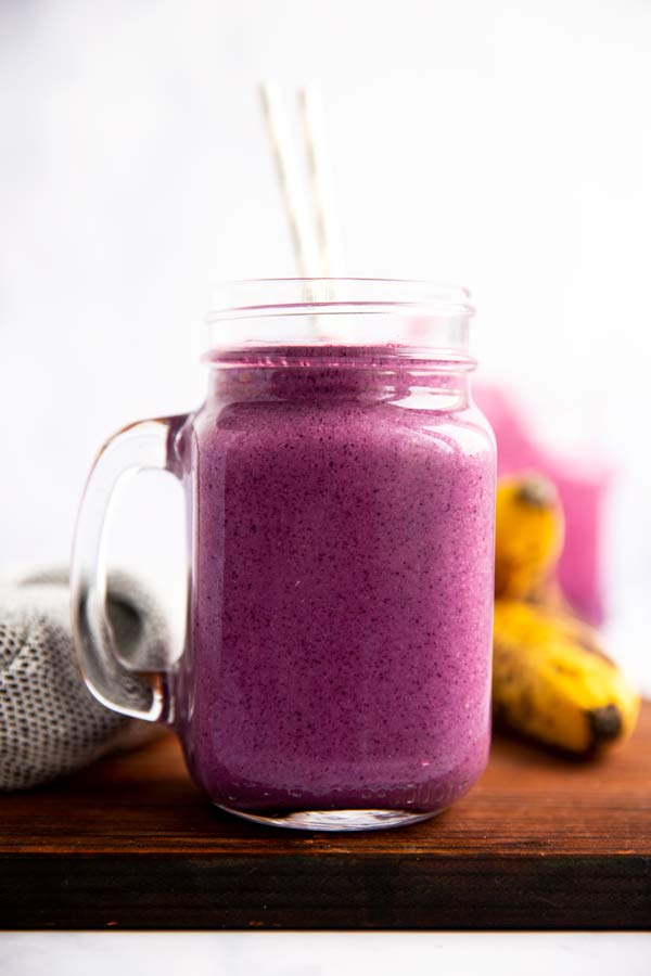 glass with purple blueberry banana smoothie on a wooden board