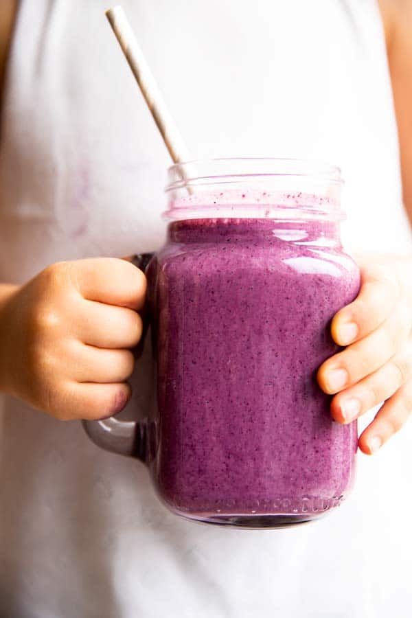 person holding a glass of blueberry smoothie
