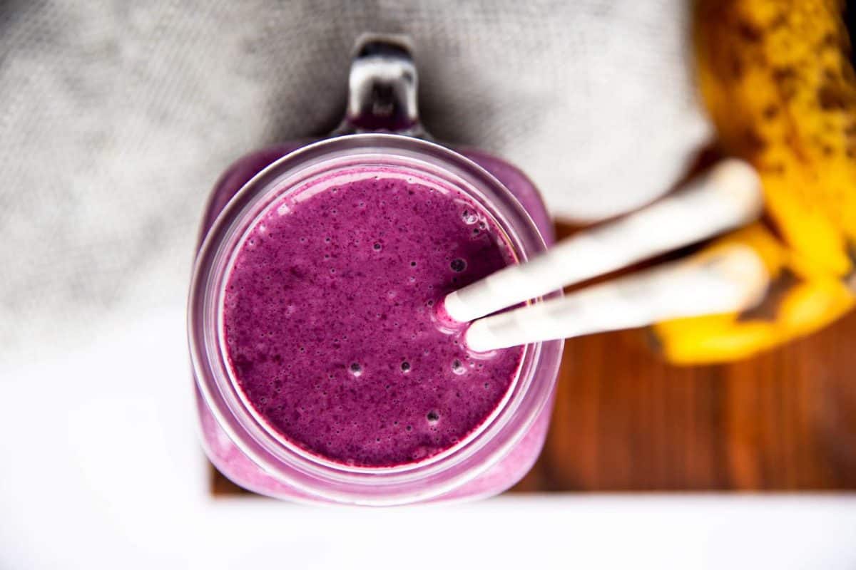 glass with purple smoothie on a wooden board next to fresh bananas