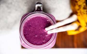 glass with purple smoothie on a wooden board next to fresh bananas