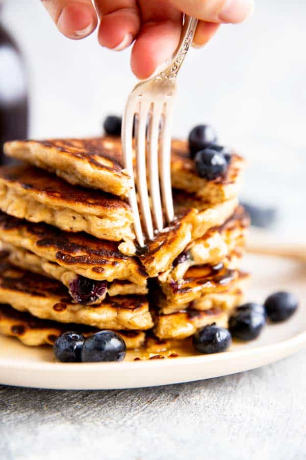 sticking a fork into a stack of blueberry oatmeal pancakes