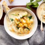 three white bowls with chicken gnocchi soup on a wooden board