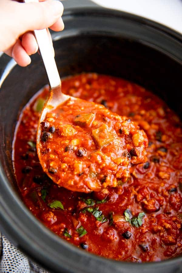 female hand holding a ladle full of chili