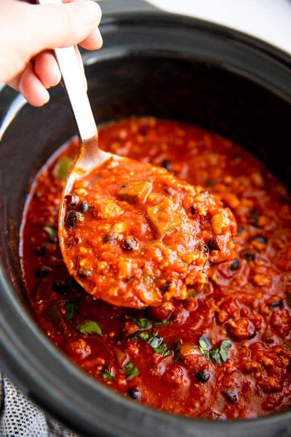 female hand holding a ladle full of chili