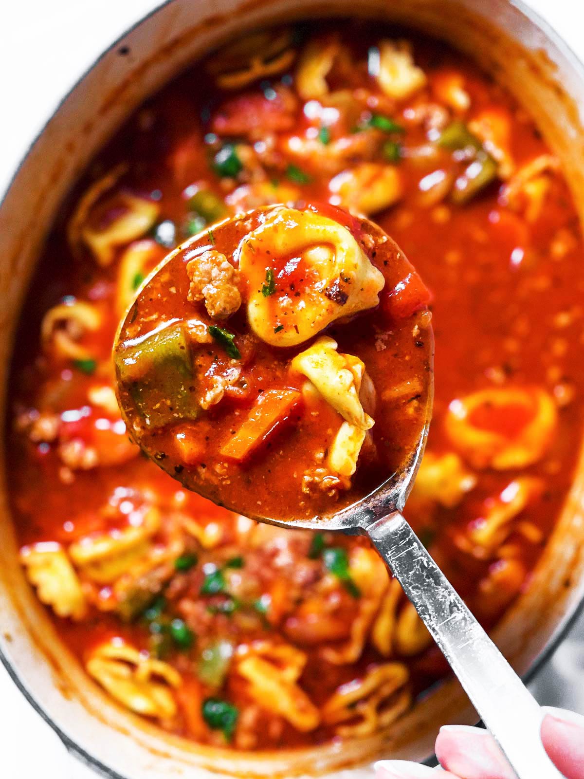 overhead view of ladle filled with sausage tortellini soup hovering over soup pot