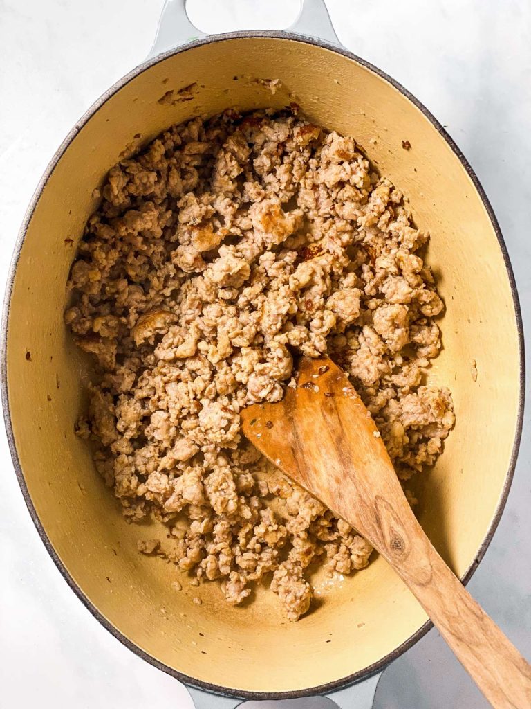 browned crumbled sausage in white Dutch oven with wooden spoon