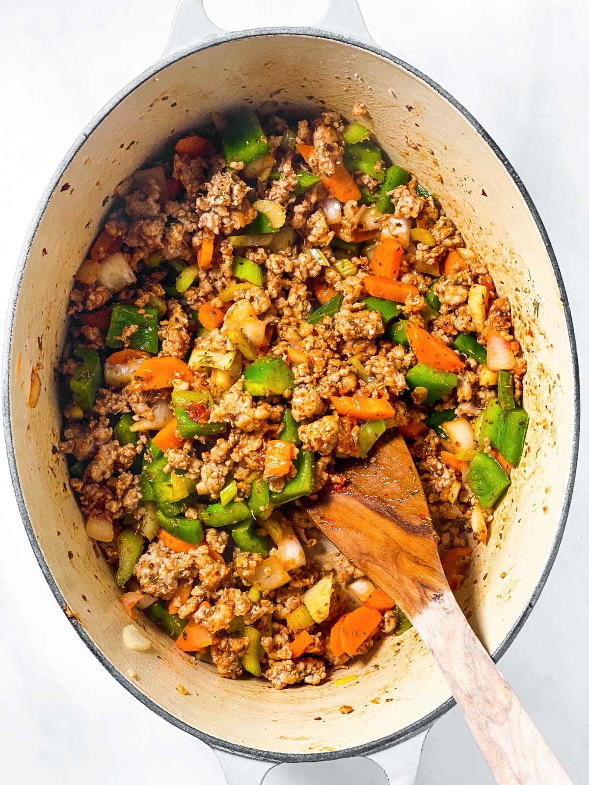 browned crumbled sausage and sautéed vegetables in white Dutch oven with wooden spoon