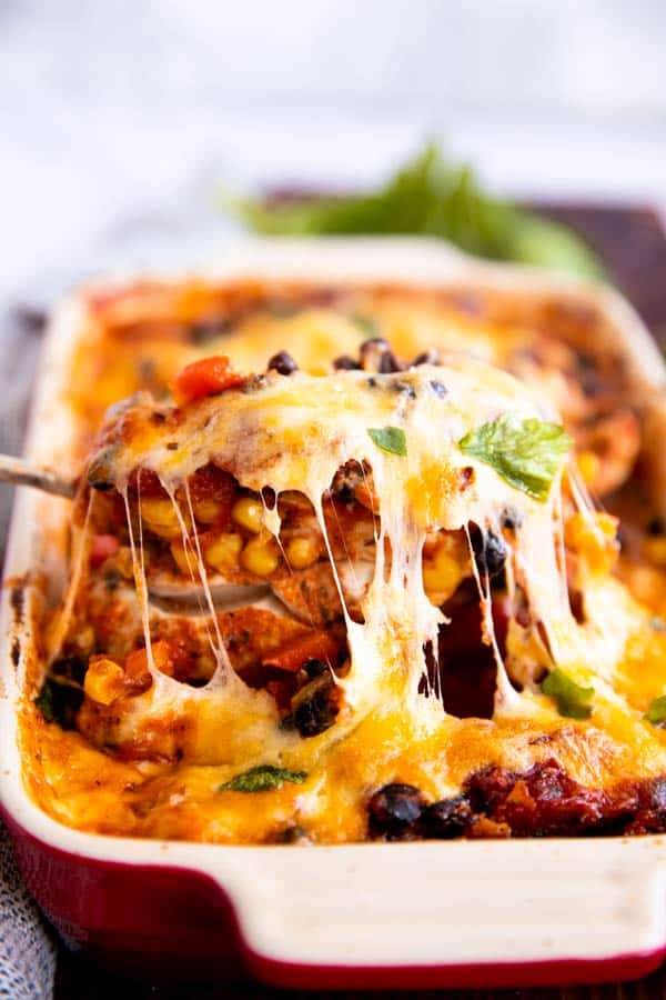 lifting a cheese covered chicken breast out of a casserole dish