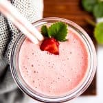 top down view of a glass with strawberry smoothie on a wooden board (vertical crop)