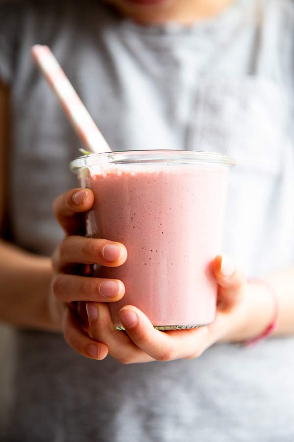 person in grey t-shirt holding a glass of strawberry smoothie