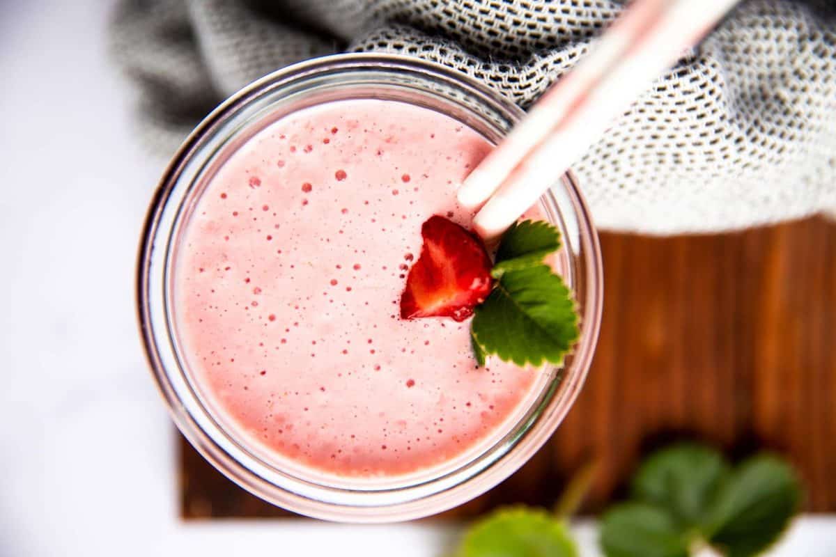 top down view of a glass with strawberry smoothie on a wooden board