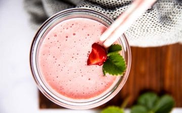 top down view of a glass with strawberry smoothie on a wooden board