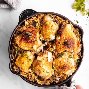female hand holding skillet with orzo and chicken thighs