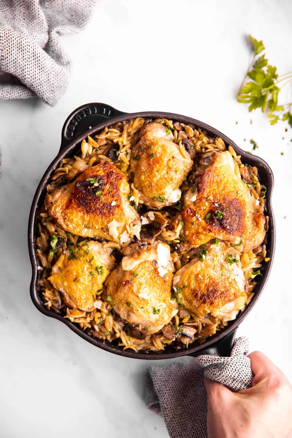 female hand holding skillet with orzo and chicken thighs