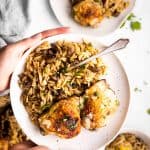 female hands holding white plate with mushroom orzo and chicken thighs