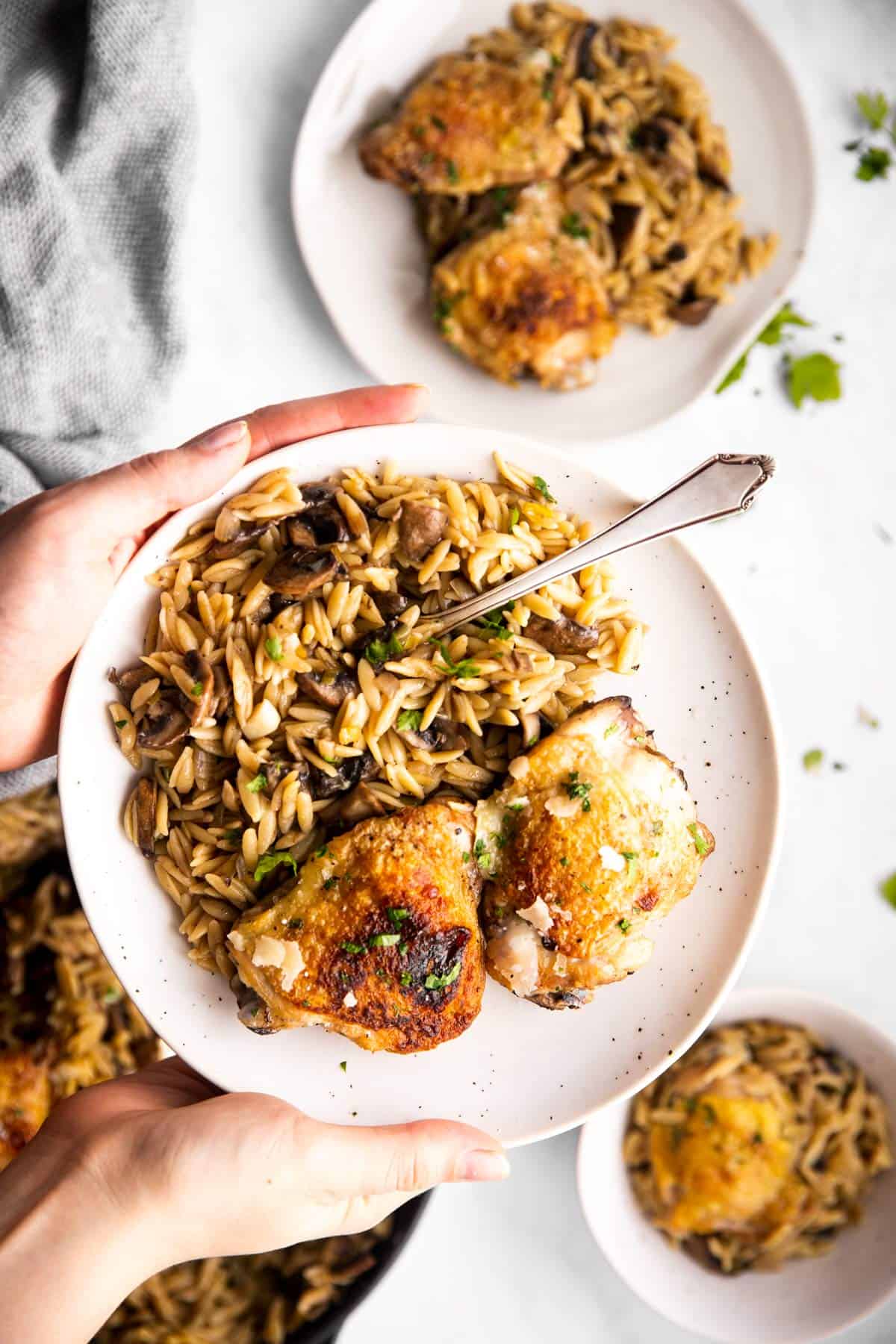 female hands holding white plate with mushroom orzo and chicken thighs