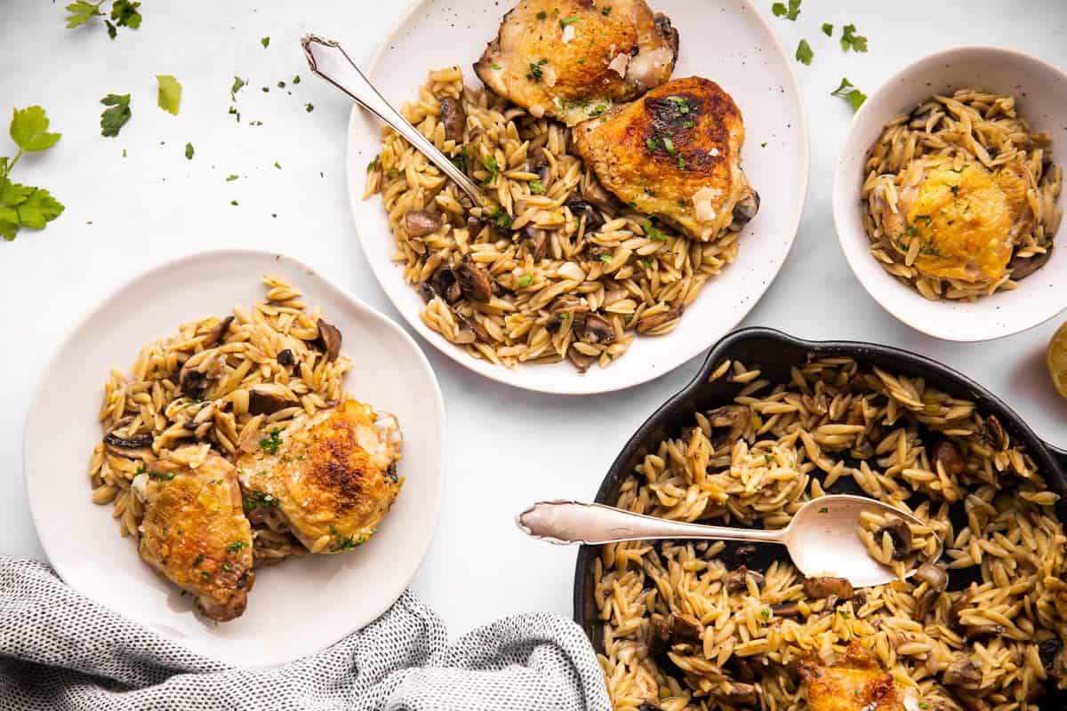 mushroom orzo and chicken skillet on white tabletop with several plates around