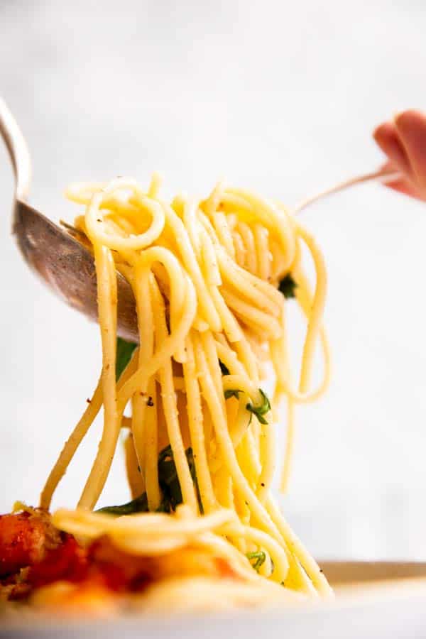 pulling up spaghetti with a fork and spoon from a plate
