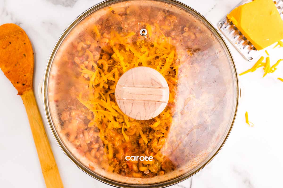 Melting cheese in pan filled with American Goulash with lid.