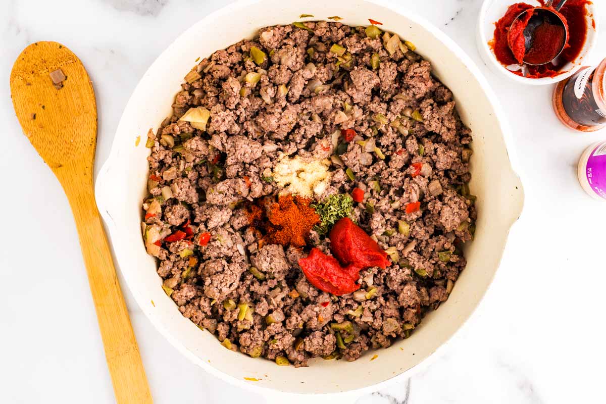 Adding aromatics to browned ground beef in skillet.