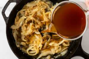 broth being poured into skillet with sautéed onions