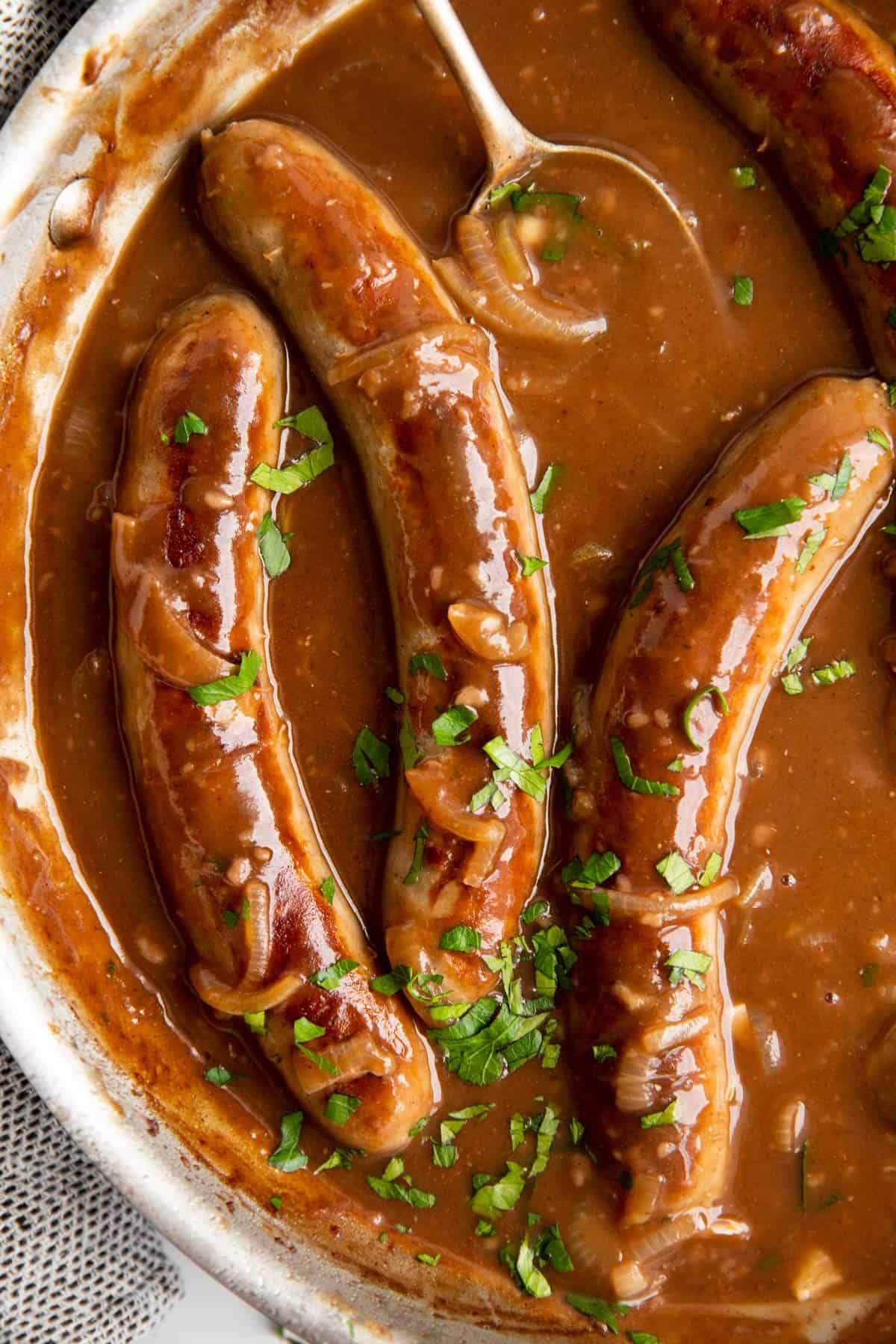 close up photo of sausage in a pan with onion gravy