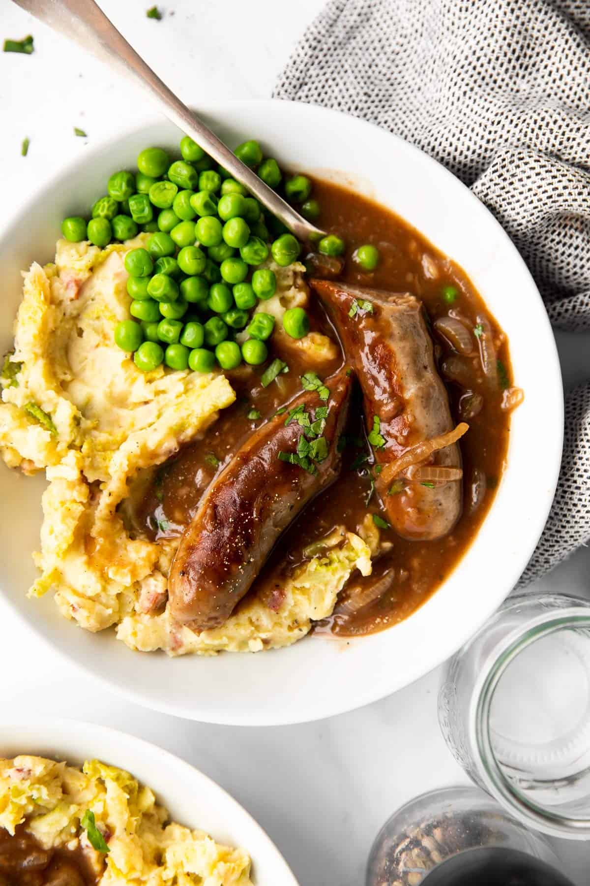 top down view of a plate with bangers and mash (sausages in onion gravy with mashed potatoes)