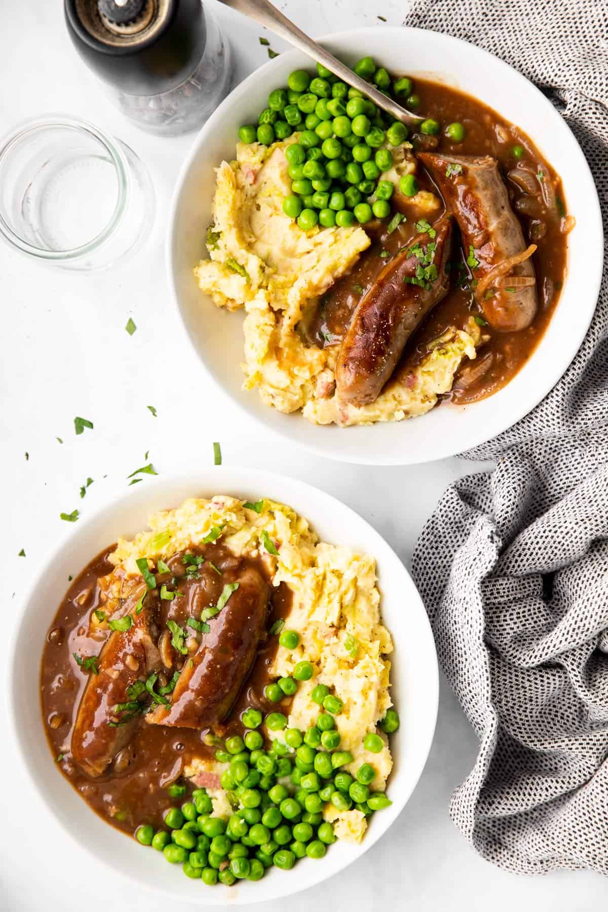 tow plates on a light surface with mashed potatoes, gravy, peas and sausages