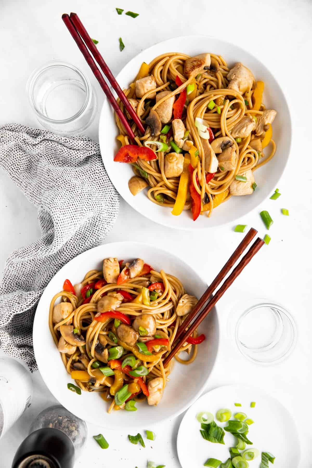 two white plates with chicken lo mein and chopsticks on a bright table