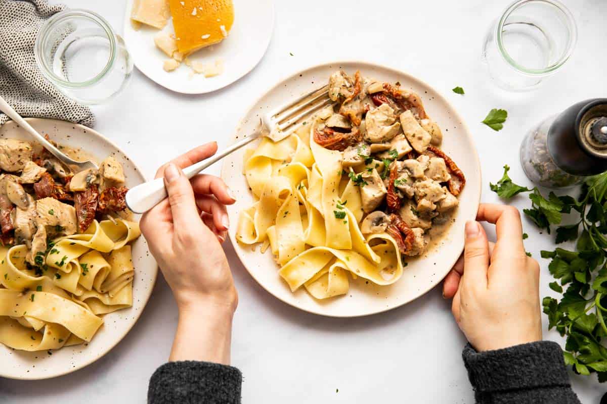 top down view on female hands holding a plate of chicken and pasta