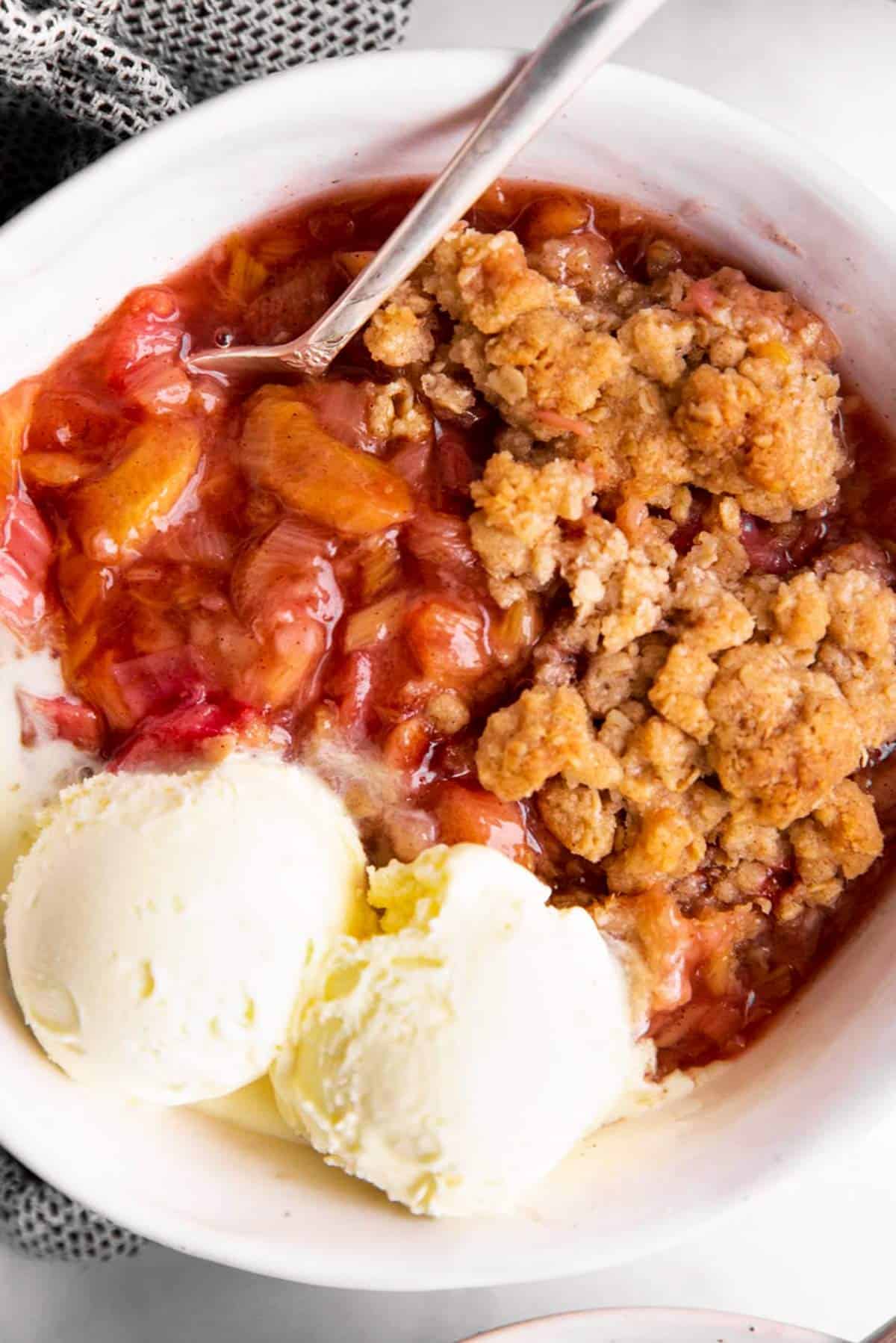 close up photo of rhubarb crisp in white bowl with vanilla ice cream