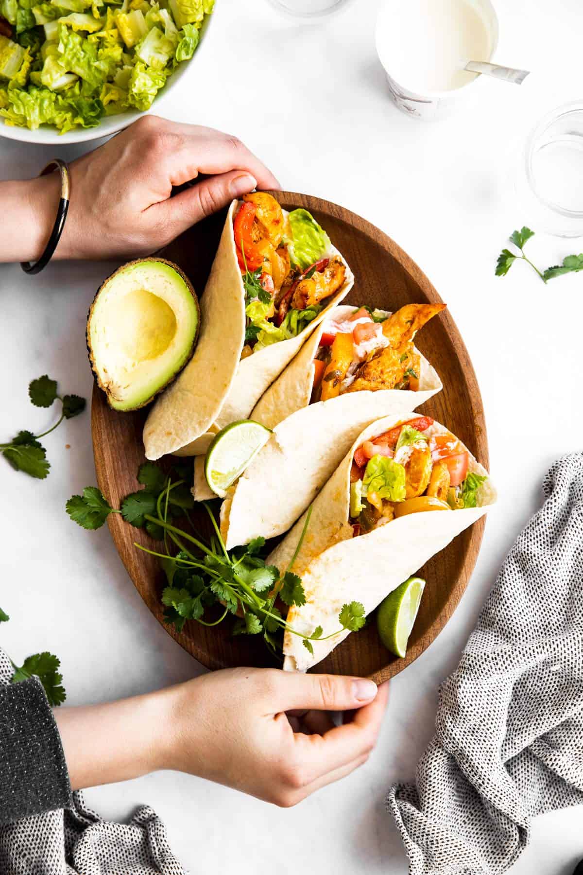 top down view on female hands holding a plate with three chicken fajitas