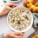 top down view on female hands holding white bowl with chicken salad next to croissants