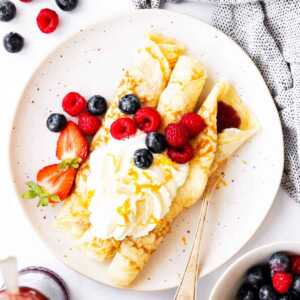 top down view on plate with crepes, whipped cream and berries