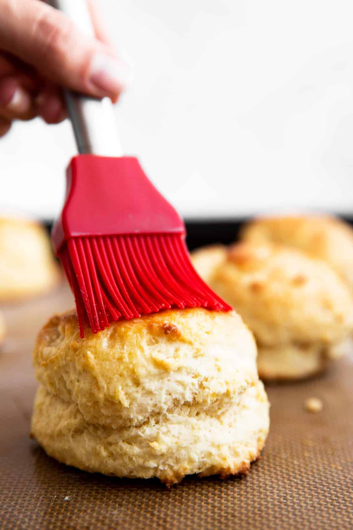 brushing the top of a biscuit with butter, using a red pastry brush